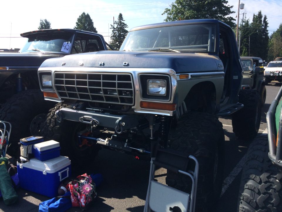 Modified Ford pickup truck with large tires and custom bumper. Another vehicle is visible to the left