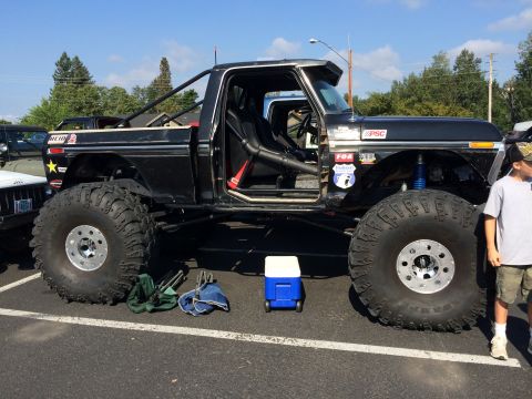 1989 Ford Bronco - A heavily modified black Ford truck with oversized tires and a roll cage sits parked at an outdoor event.