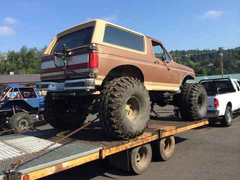 1989 Ford Bronco - A lifted 1989 Ford Bronco is transported on a flatbed trailer, accompanied by another vehicle.