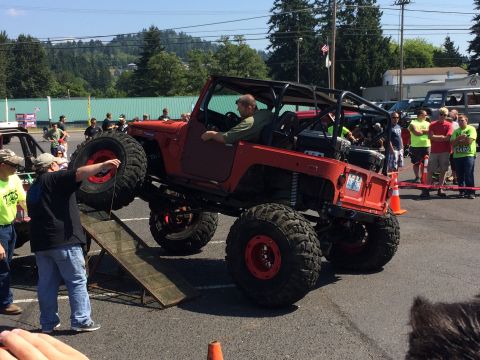 1989 Ford Bronco - A red Jeep with oversized tires is positioned on a ramp during an outdoor event.