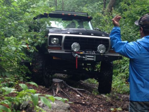1979 Ford Bronco - This 1979 Ford Bronco is shown off-roading through a wooded area, with a person in a blue jacket visible to the right.