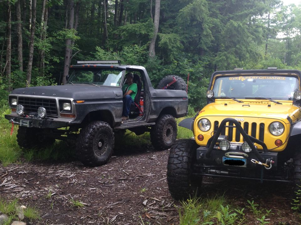 1979 Ford Bronco and a yellow Jeep parked on a dirt path in a wooded area