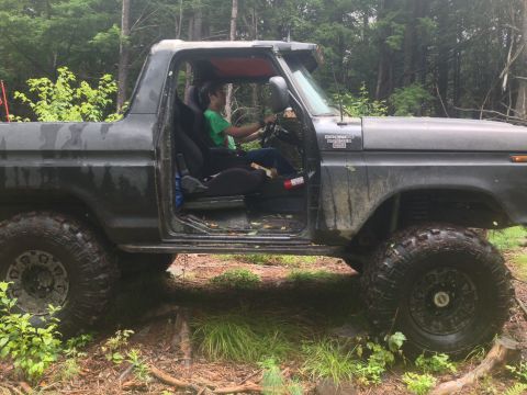 1979 Ford Bronco - A person drives a 1979 Ford Bronco through a wooded area, with the driver's side door open.