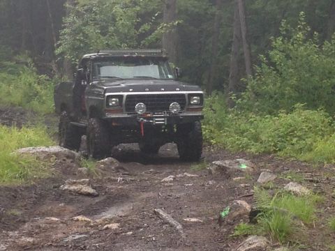 1979 Ford Bronco - This lifted Ford truck navigates a challenging, rocky, and muddy off-road path surrounded by dense forest foliage.