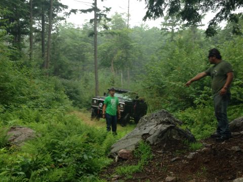 1979 Ford Bronco - Two men stand near an off-road vehicle partially obscured by foliage in a wooded area.