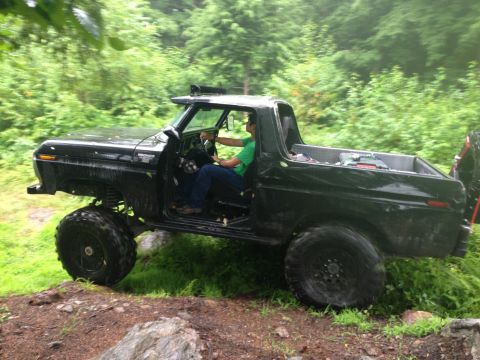 1979 Ford Bronco - A black 1978 Ford Bronco navigates a rocky, wooded trail with its driver visible.