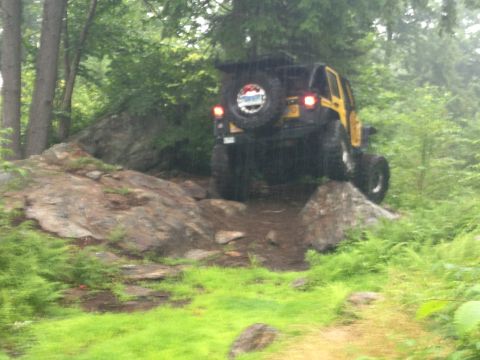 1979 Ford Bronco - A yellow Jeep Wrangler navigates a rocky off-road trail in a wooded area.