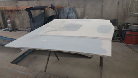 1991 Ford LTD Crown Victoria - A car hood, prepped for paint, rests on a stand in a garage setting.