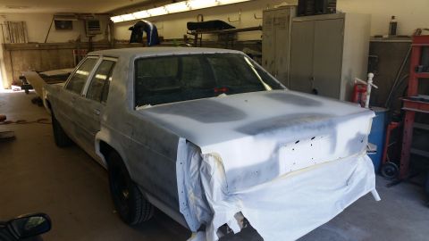 1991 Ford LTD Crown Victoria - A sedan in a body shop, covered in primer and masking tape, awaits refinishing.