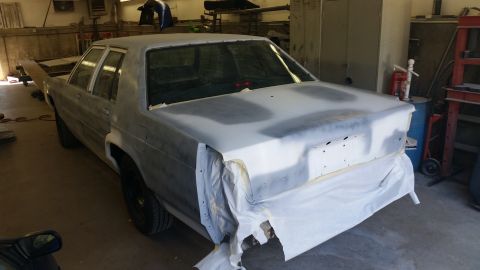 1991 Ford LTD Crown Victoria - A sedan in a workshop is covered in primer and masking paper, indicating it is undergoing repairs or a paint job.