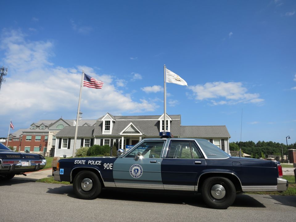 Blue State Police 90E sedan parked outside museum building