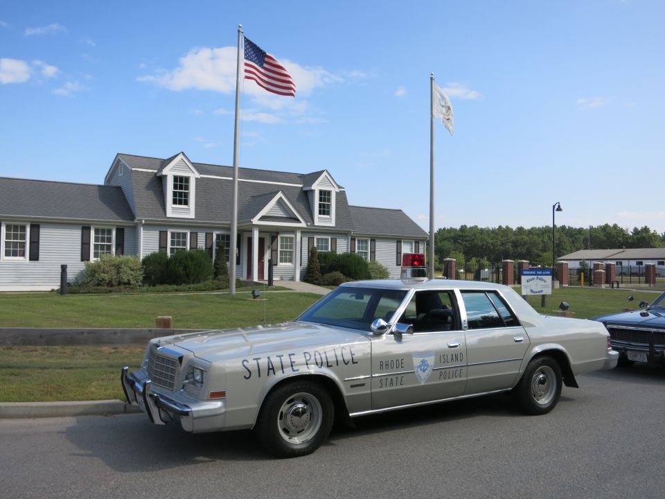 Silver Rhode Island State Police sedan parked under flag