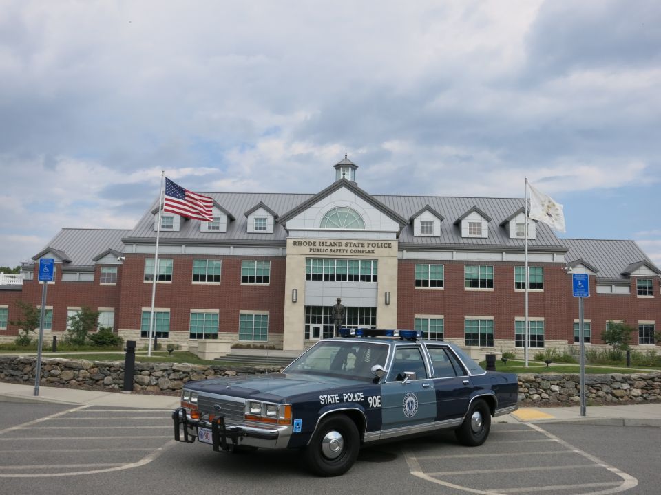 Blue State Police 90E sedan parked before Rhode Island State Police brick building