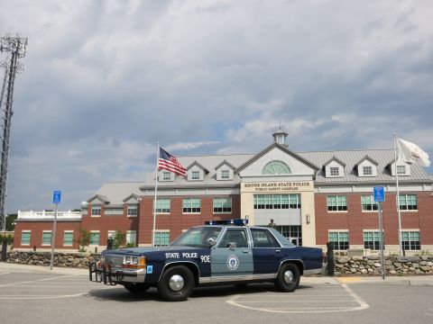 1991 Ford LTD Crown Victoria - blue State Police 90E sedan parked in front of the Rhode Island State Police Public Safety Complex with a cell tower at left.
