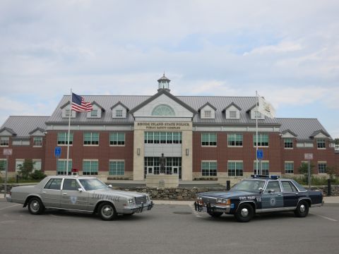 1991 Ford LTD Crown Victoria - silver State Police sedan and a blue State Police sedan parked side by side facing the camera before the Rhode Island State Police complex.