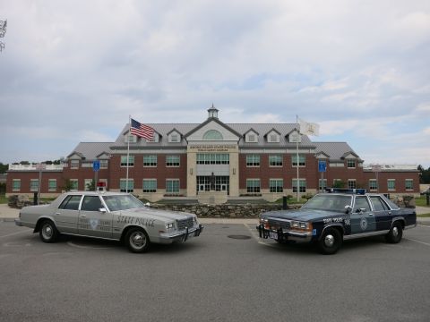 1991 Ford LTD Crown Victoria - silver State Police sedan and a blue State Police sedan parked at slight angles before the Rhode Island State Police Public Safety Complex.