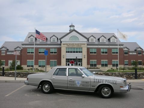 1991 Ford LTD Crown Victoria - silver Rhode Island State Police sedan with a roof light bar parked in profile in front of the State Police Public Safety Complex.