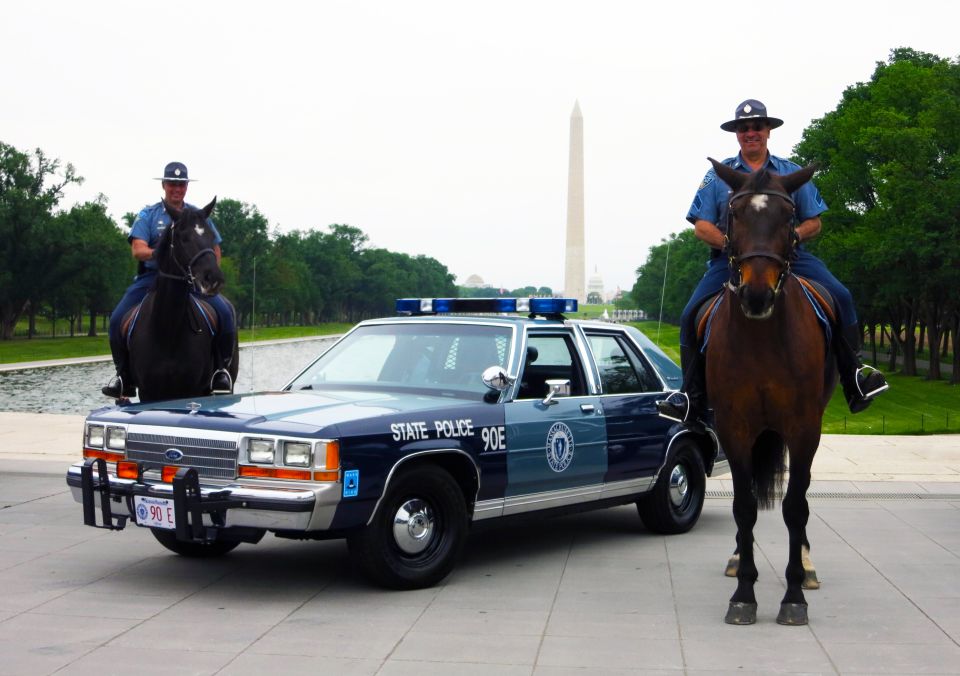 Blue State Police 90E sedan flanked by two mounted officers near Washington Monument