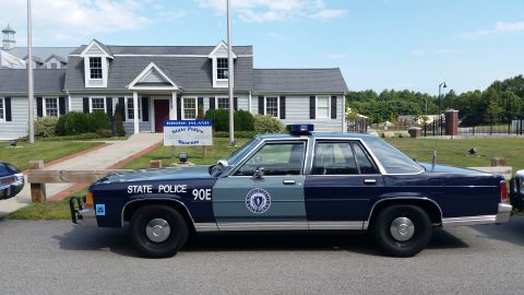 1991 Ford LTD Crown Victoria - blue State Police 90E sedan parked in profile outside the white-sided Rhode Island State Police Museum building.