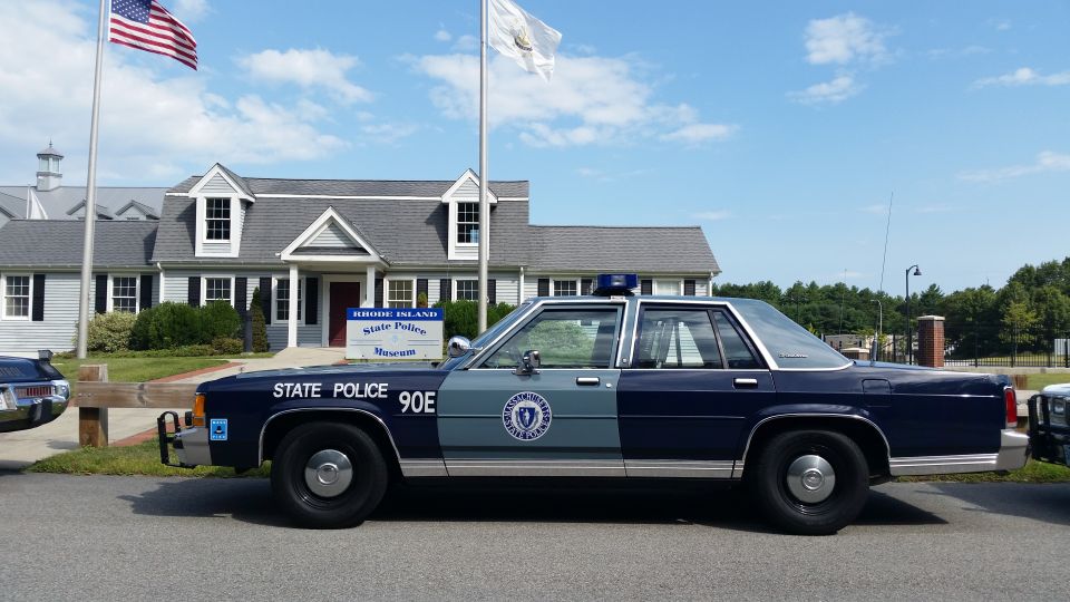 Blue State Police 90E sedan in profile by flags at State Police Museum