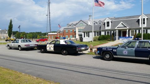 1991 Ford LTD Crown Victoria - lineup of police cars, including a silver sedan, a black-and-white cruiser and a blue 90E sedan, parked outside the State Police Museum.