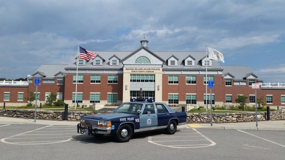 Blue and grey 1991 Ford Crown Victoria police car parked in front of a brick building with flags