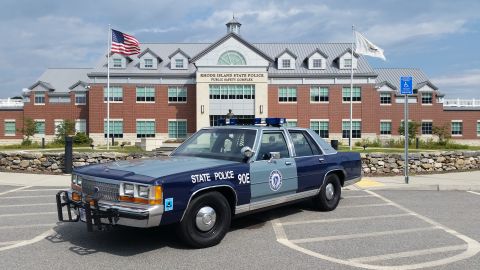 1991 Ford LTD Crown Victoria - A 1991 Ford Crown Victoria police car, marked 'STATE POLICE 90E', is parked in front of the Rhode Island State Police Public Safety Complex.