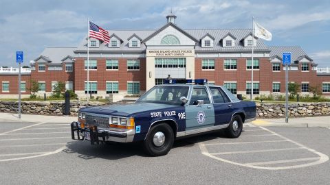 1991 Ford LTD Crown Victoria - A police car with 'STATE POLICE' text on its side is parked in front of the Rhode Island State Police Public Safety Complex.