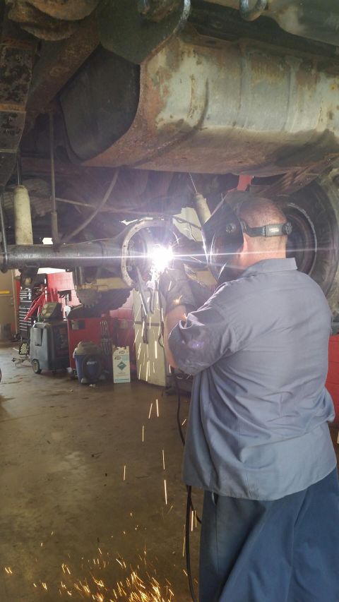 1986 Ford Bronco - A mechanic works on the undercarriage of a vehicle, welding the rear axle.