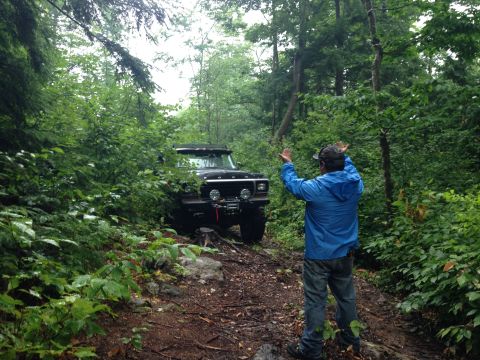 1979 Ford Bronco - A person directs a black 1978 Ford Bronco navigating a wooded trail.