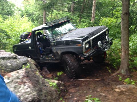 1979 Ford Bronco - This modified Ford Bronco is navigating a challenging off-road course with large rocks and trees.