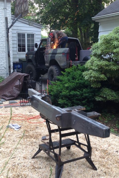 1979 Ford Bronco - A person is welding on the bed of a camouflaged Ford Bronco in a residential yard.