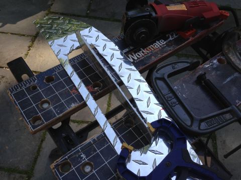 1979 Ford Bronco - Cutting diamond plate metal with an angle grinder and clamps on a workbench.