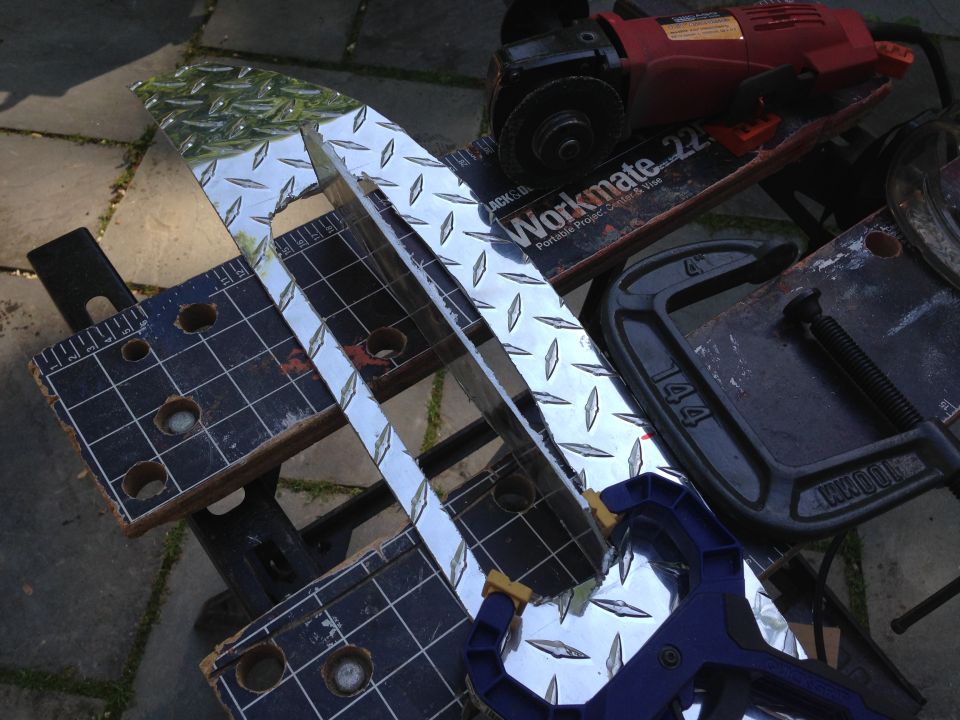 Diamond plate metal strips clamped to a workbench, with an angle grinder and clamps nearby