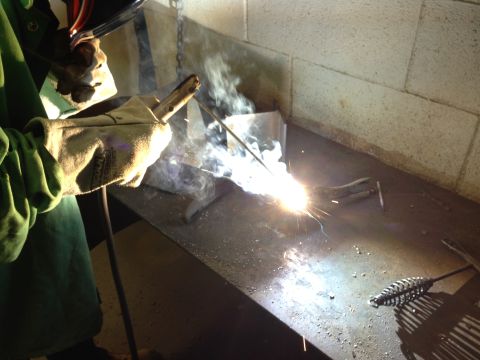 1979 Ford Bronco - A person is welding metal on a workbench, creating sparks and smoke.