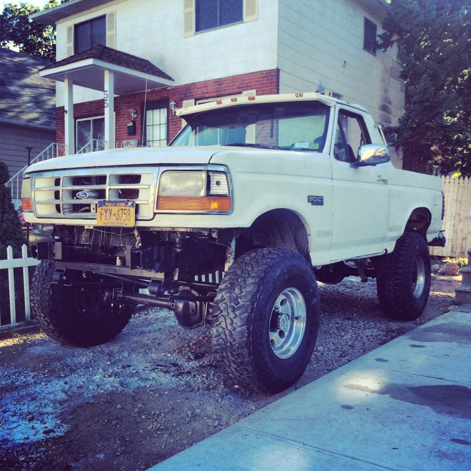 White Ford Bronco with lifted suspension and large tires parked in front of a house