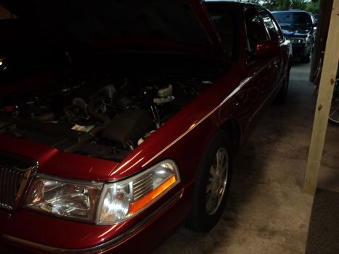 2004 Mercury Grand Marquis - A red 2004 Mercury Grand Marquis is parked in a garage with its hood up, next to another vehicle.