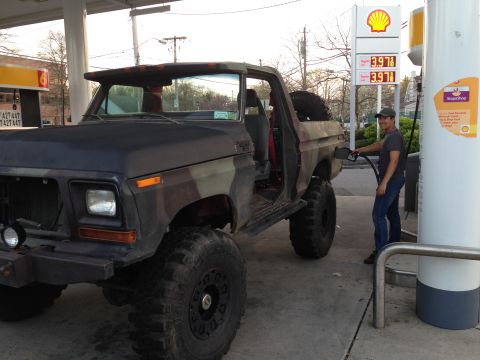 1979 Ford Bronco - Man fueling a lifted 1979 Ford Bronco with camouflage paint at a gas station.
