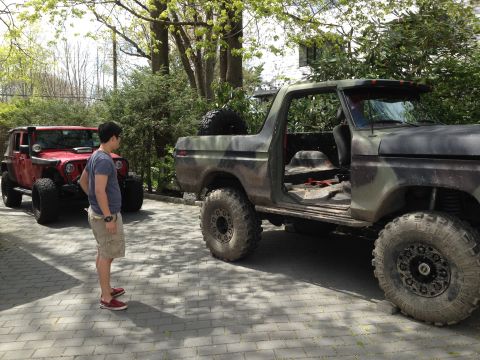 1979 Ford Bronco - Two off-road vehicles, a Ford Bronco and a Jeep Wrangler, are parked on a paved driveway.