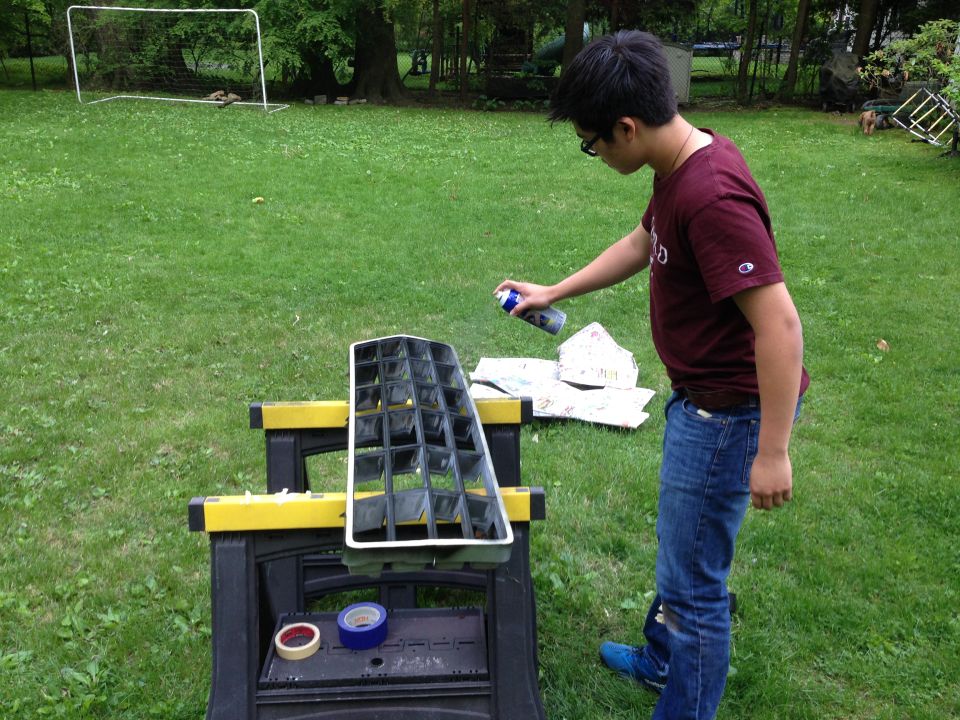Black and chrome car grille on sawhorses, being spray painted by a person