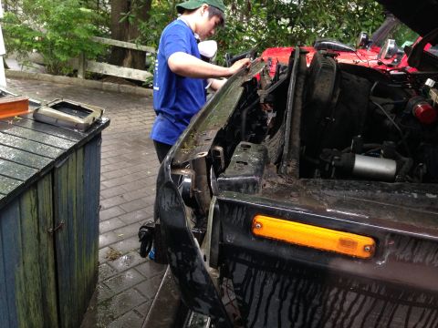 1979 Ford Bronco - A person works on the front end of a black vehicle, possibly a truck or SUV, with the hood open.
