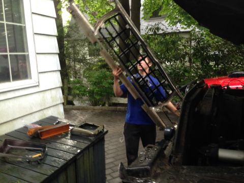 1979 Ford Bronco - Man removes a large metal grille part from a vehicle.