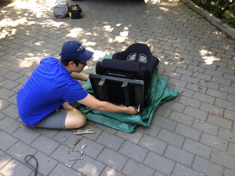 1979 Ford Bronco - A person is shown kneeling on a paver driveway, working on a car seat that is placed on a green tarp.