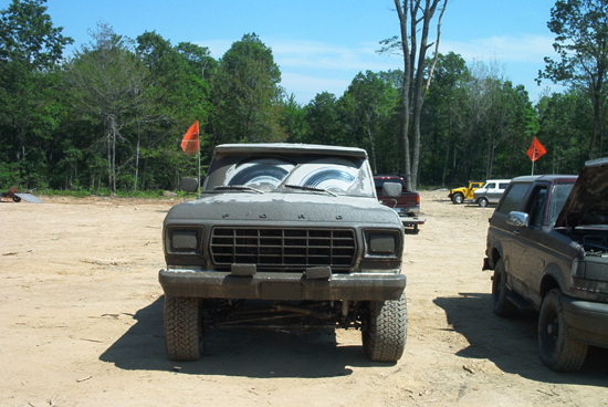 Front view of a dusty 1979 Ford F-Series truck with a large grille and off-road tires. Other vehicles are parked nearby