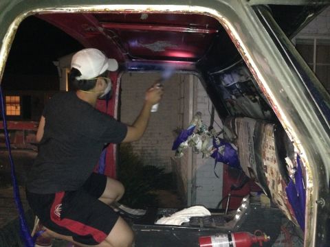 1979 Ford Bronco - A person is seen spraying the interior of a vehicle, revealing red and black panels and some debris.