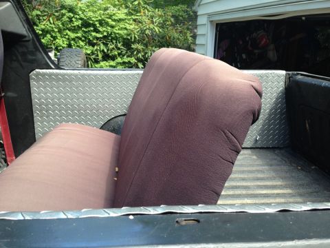 1979 Ford Bronco - Rear seats are loaded into the bed of a pickup truck, next to a garage.