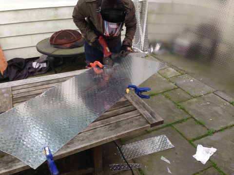 1979 Ford Bronco - A person is using an angle grinder to cut a piece of diamond plate metal on a table outside.