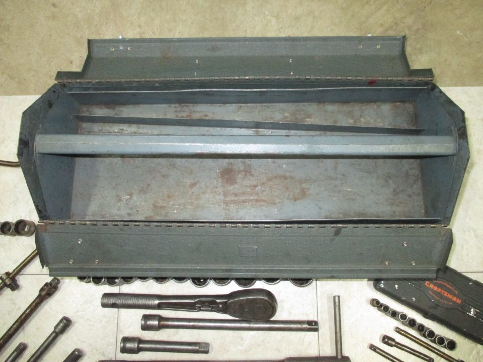 Open gray metal toolbox with a set of sockets and a ratchet wrench laid out in front