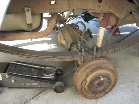 1994 Ford Bronco - The rear suspension and axle assembly of a vehicle are shown, with a floor jack supporting the frame.