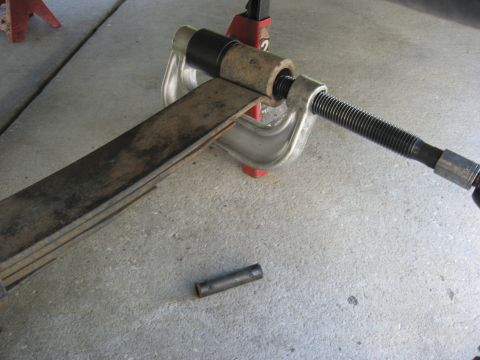 1994 Ford Bronco - A C-clamp is used to compress a leaf spring, with a small metal cylinder nearby.